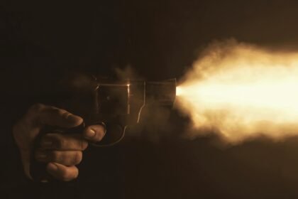 Close-up of a handgun firing with a bright flash in a dark setting, creating a dramatic effect.