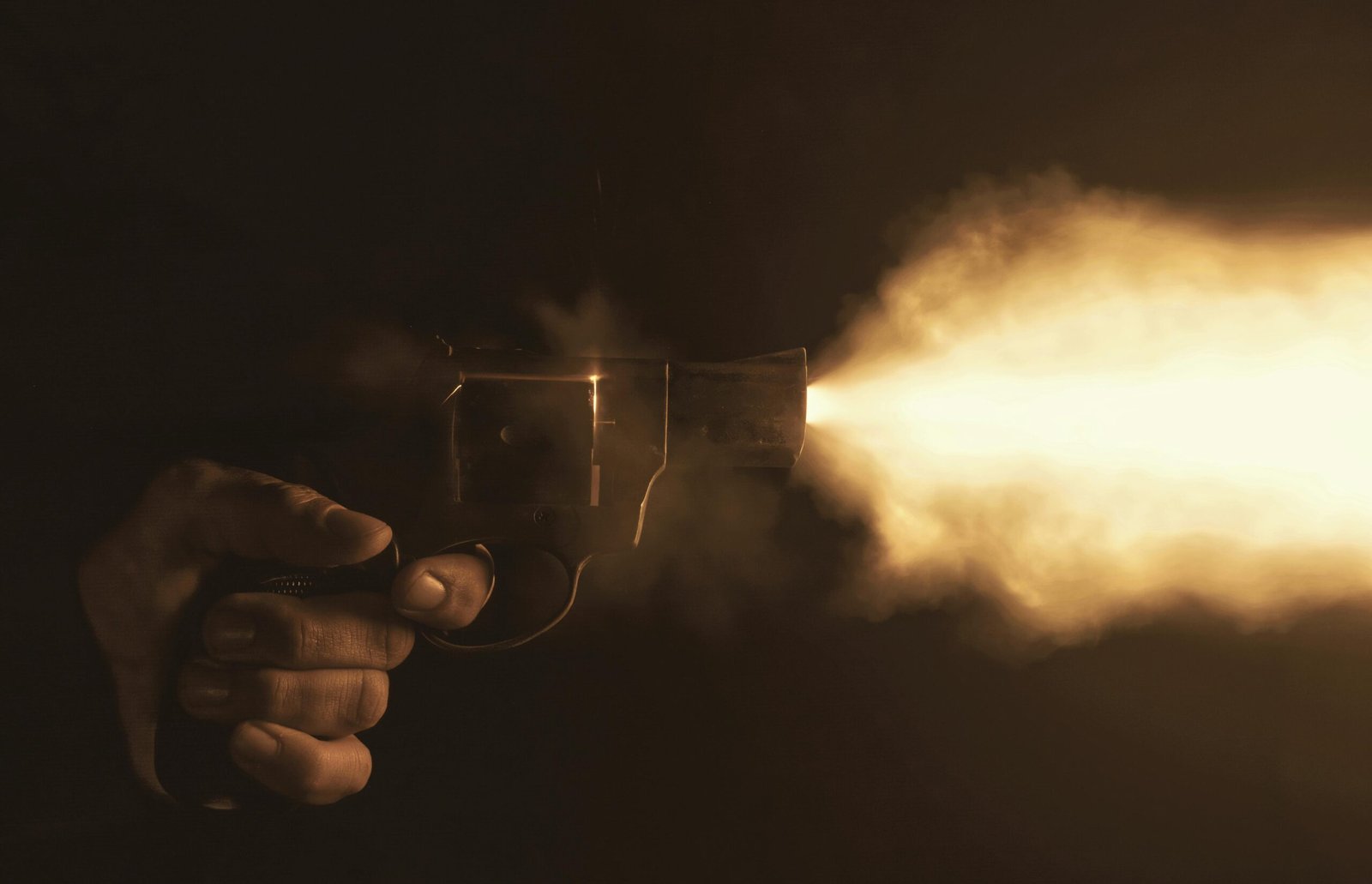 Close-up of a handgun firing with a bright flash in a dark setting, creating a dramatic effect.
