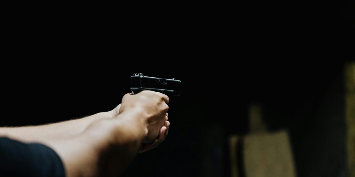 Arm aiming a handgun in a dark environment, showcasing focus and control.